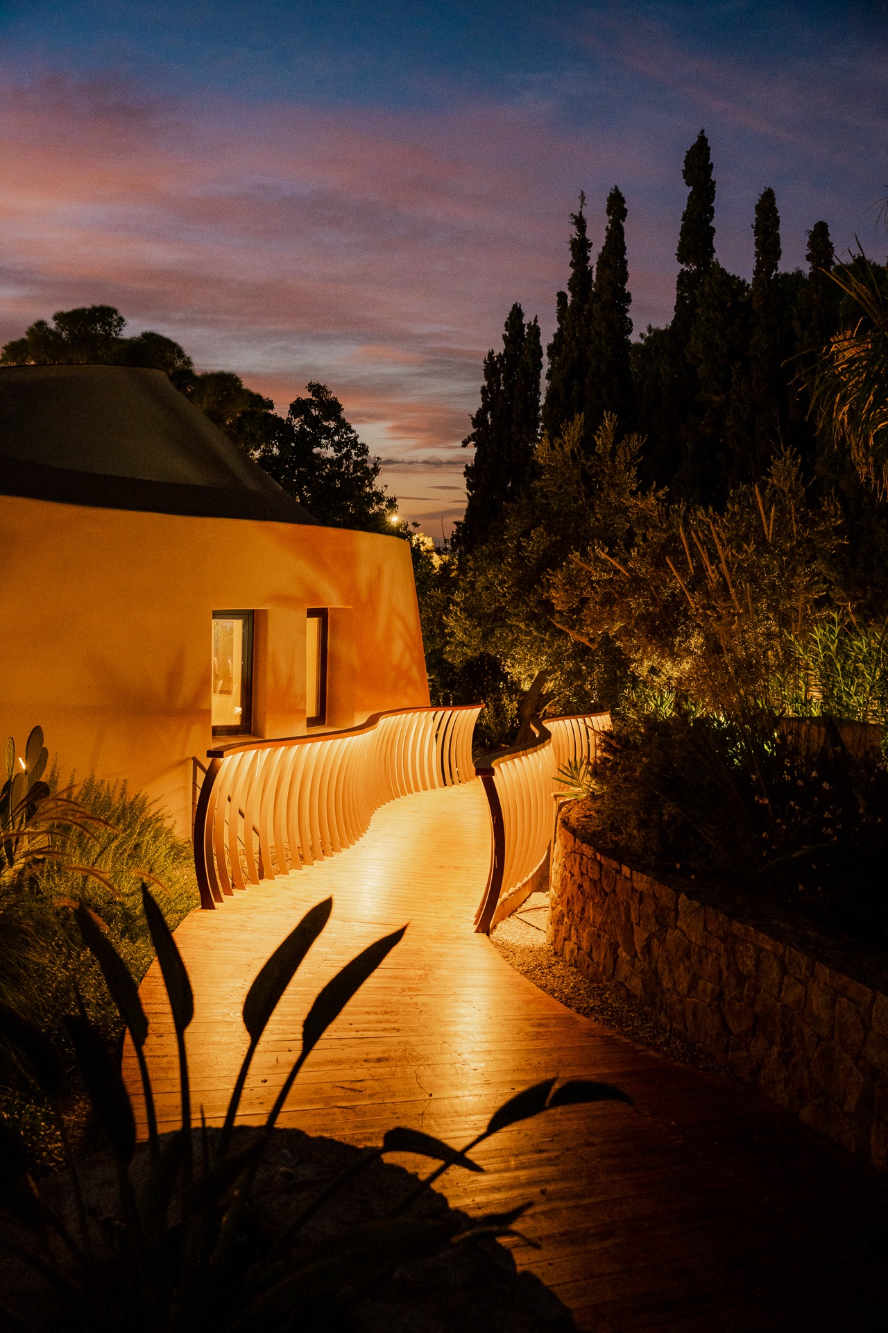 Lit walkway at dusk, curved walls and Mediterranean planting
