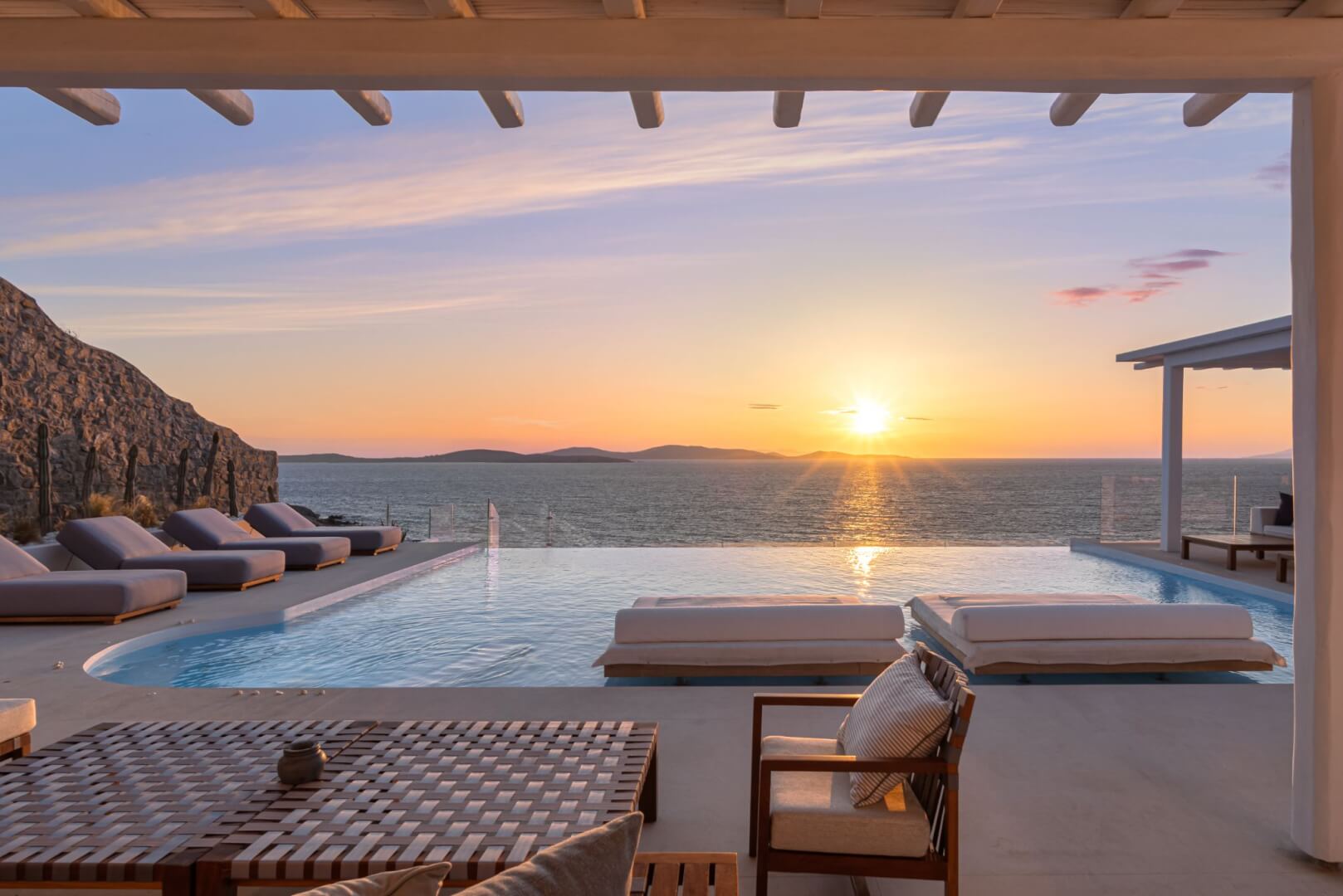 Sun loungers and infinity pool, the sun setting over the Aegean