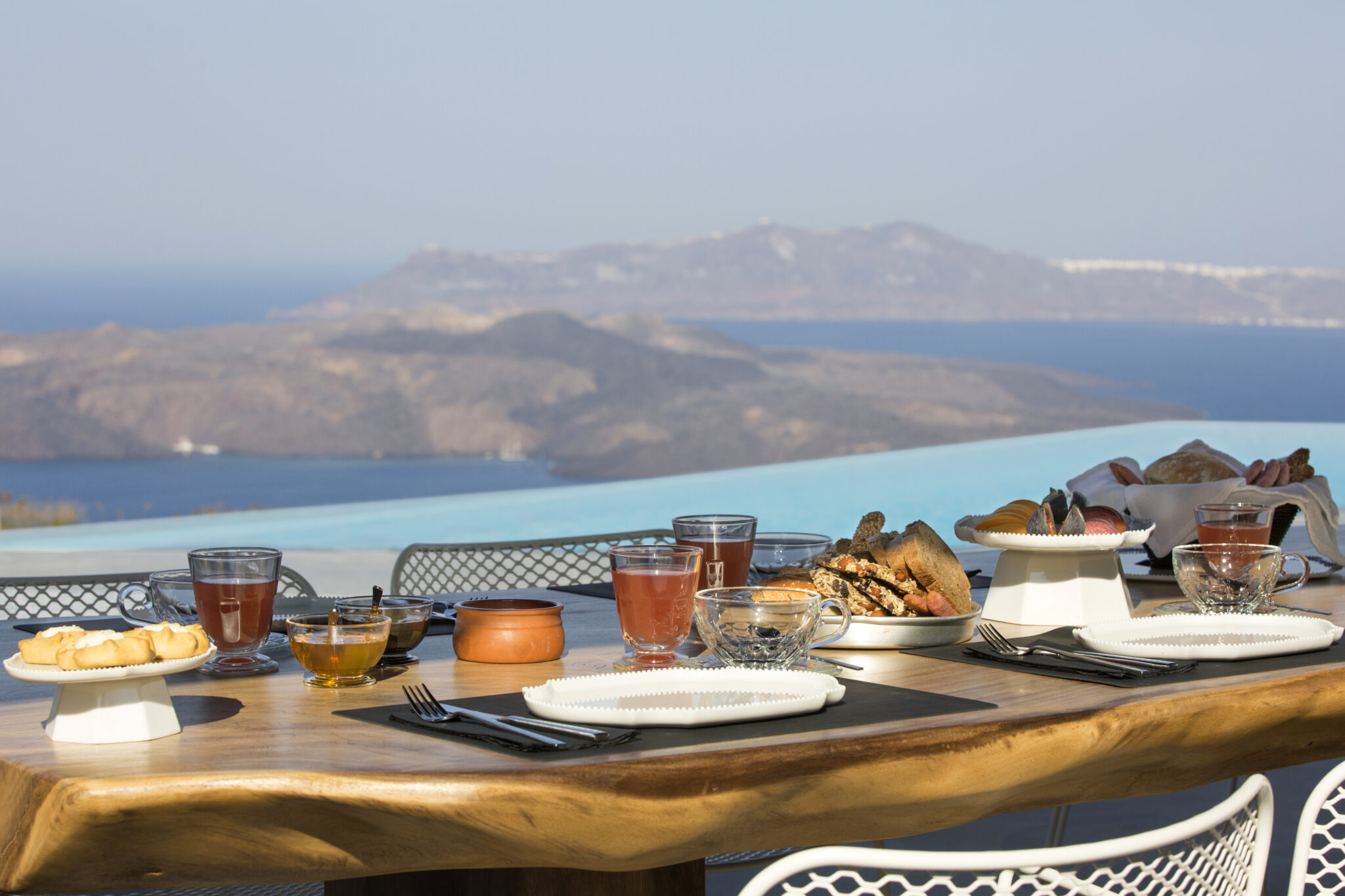 Breakfast table set on the terrace, caldera and Aegean opening behind