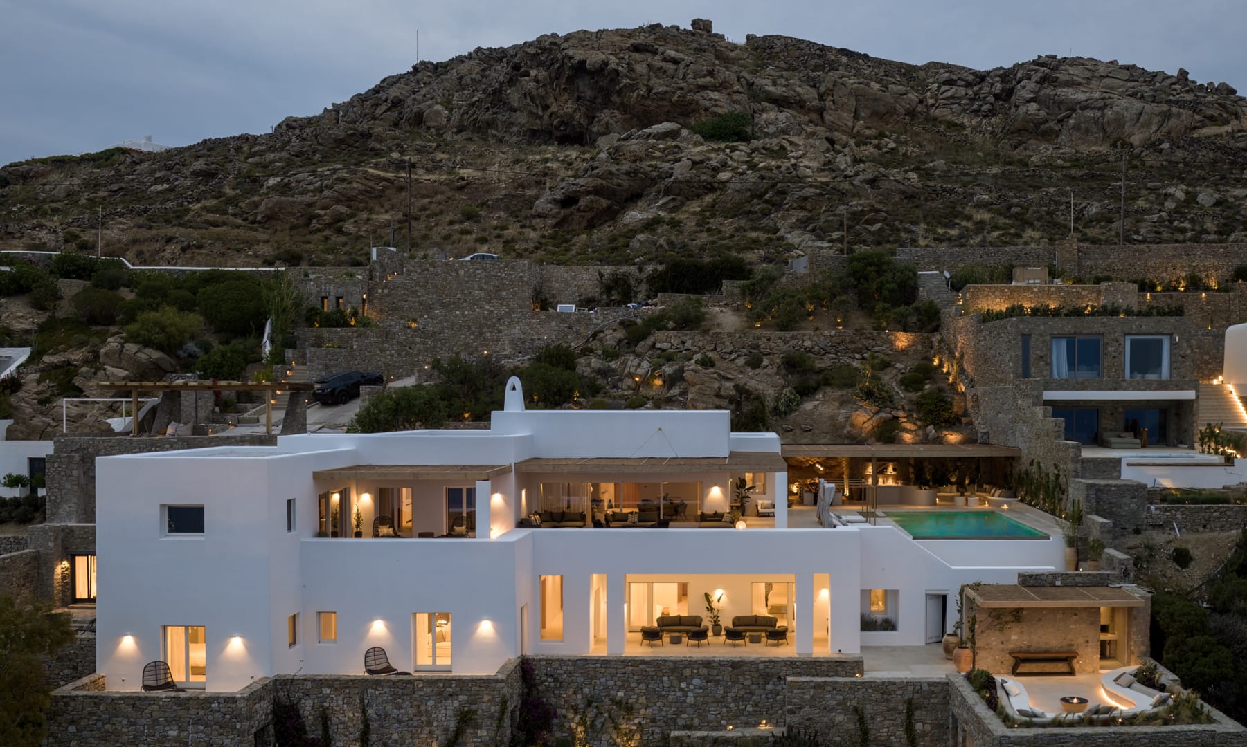 Villa Tourlos Breeze illuminated at twilight against the Mykonian hillside