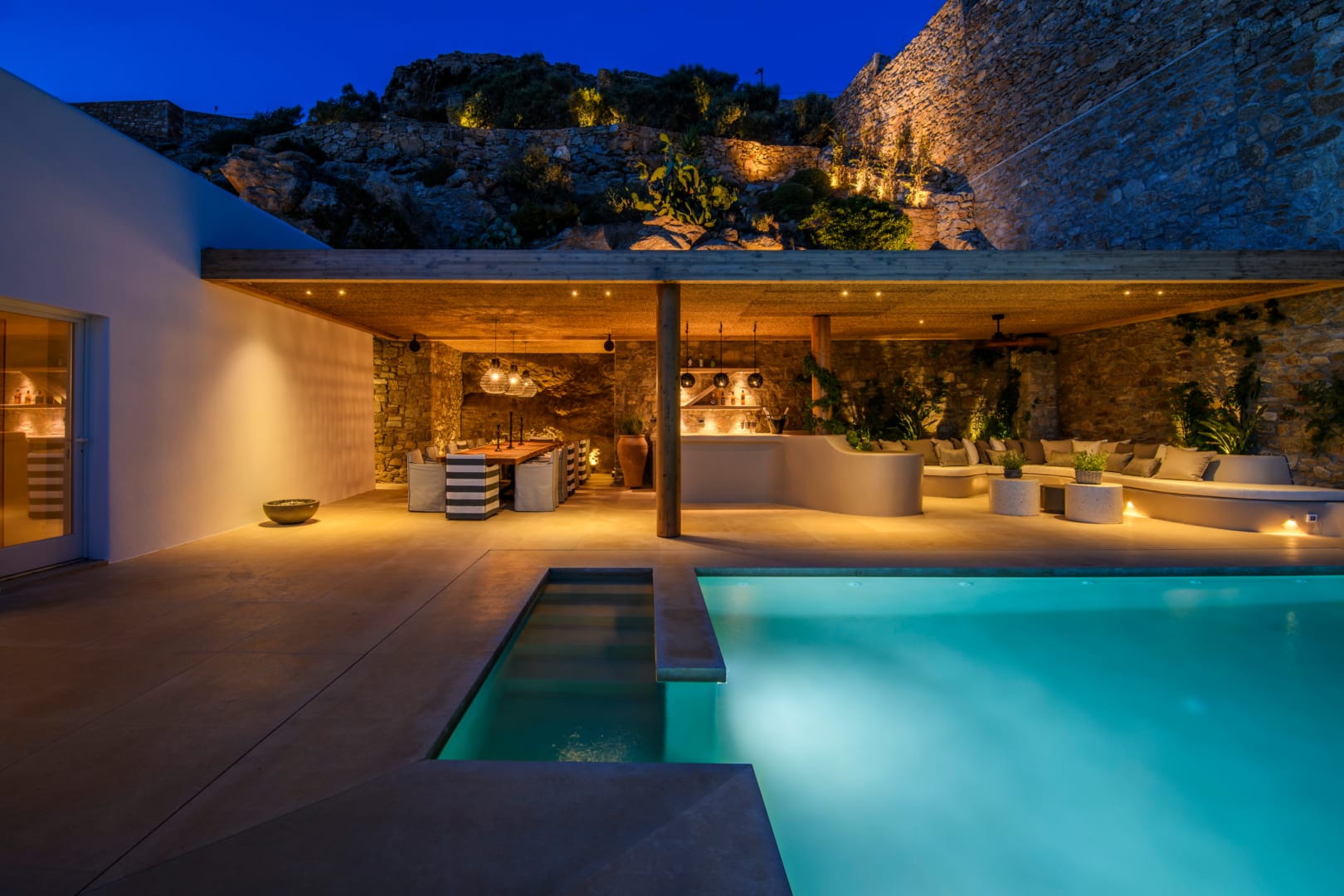 Outdoor kitchen and dining area at twilight beside the pool
