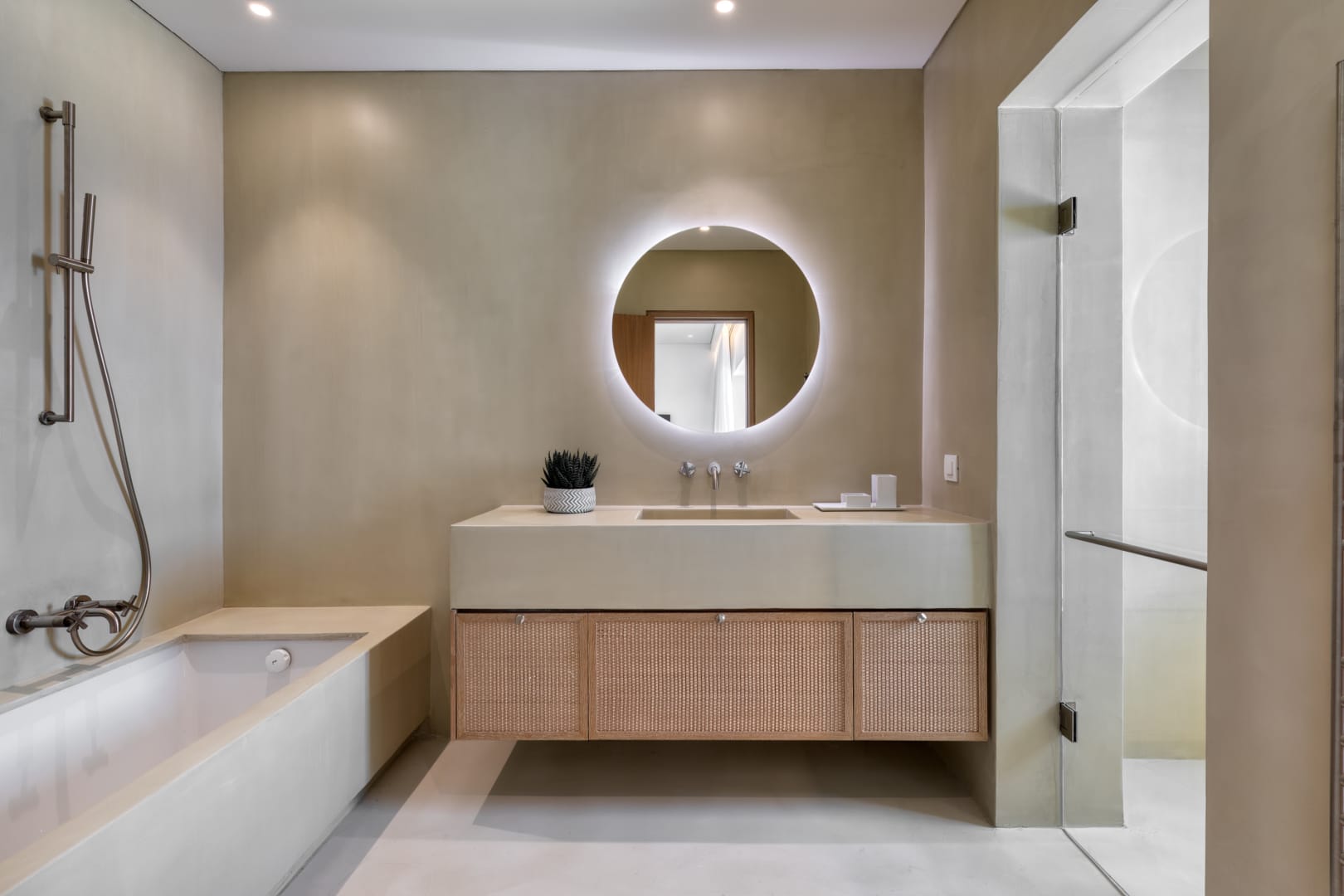 Earth-toned bathroom with circular backlit mirror and rattan vanity