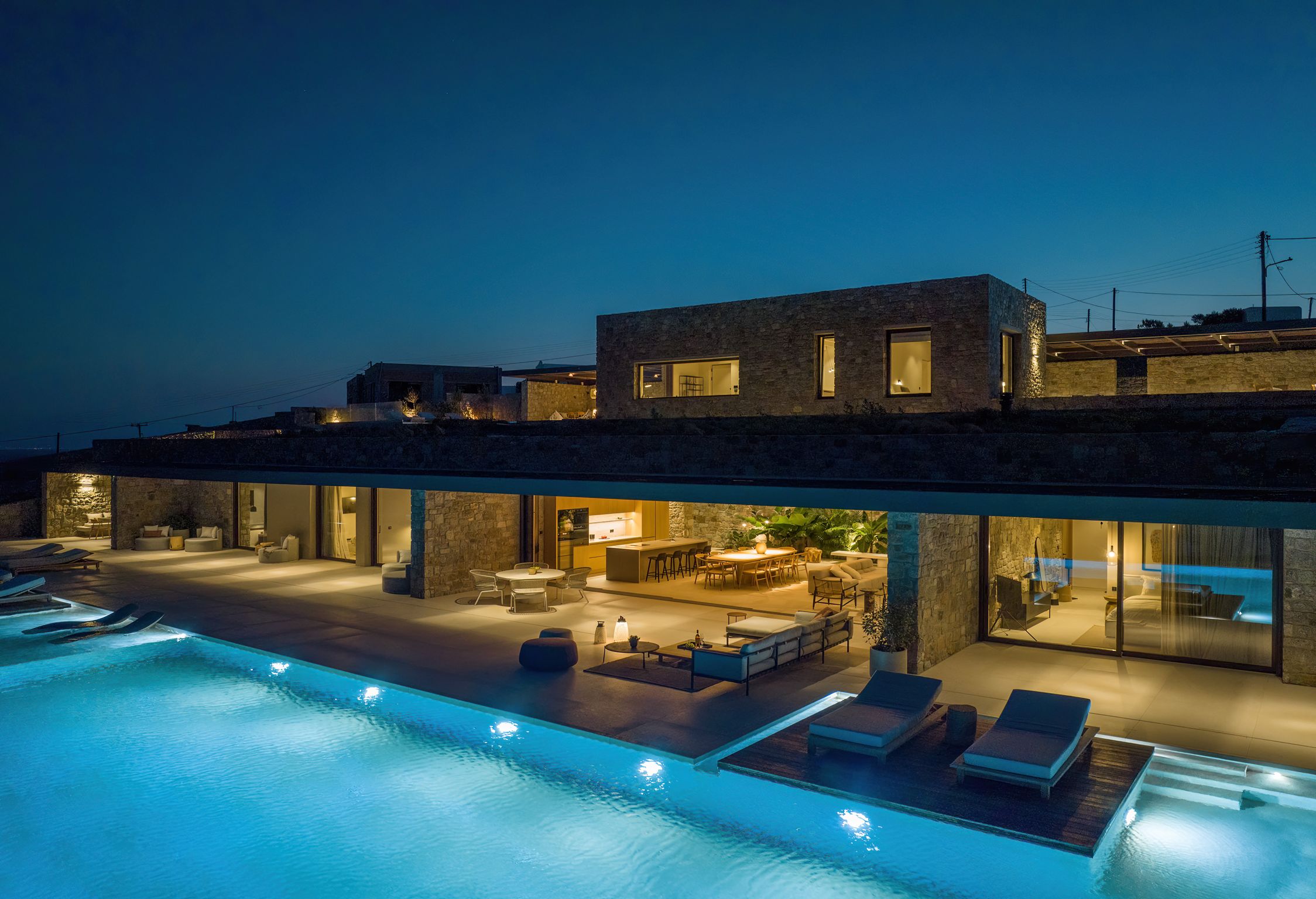 The villa illuminated at dusk, pools and open kitchen glowing